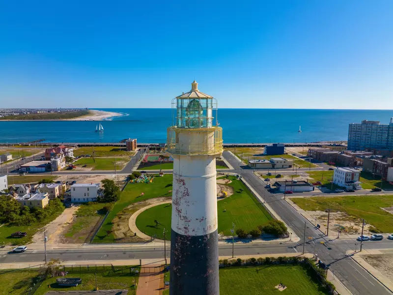 View of the Absecon Lighthouse with buildings, grass, trees and water in the background