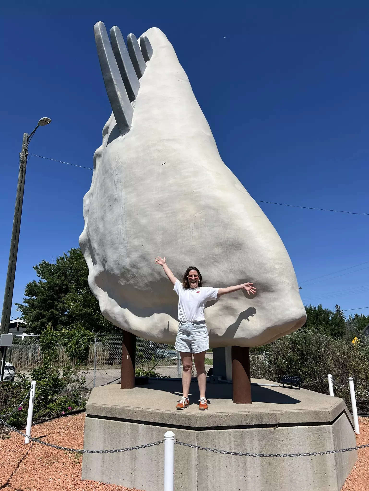 A woman poses in front of a large sculpture of a dumpling with a fork through it that towers above her