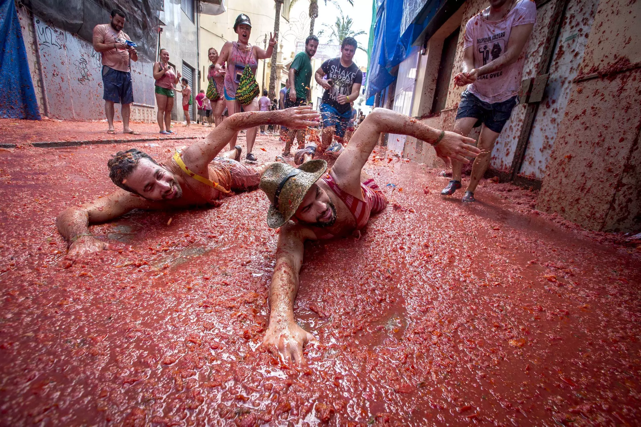 Two men lie on the ground and pretend to swim in tomatoes