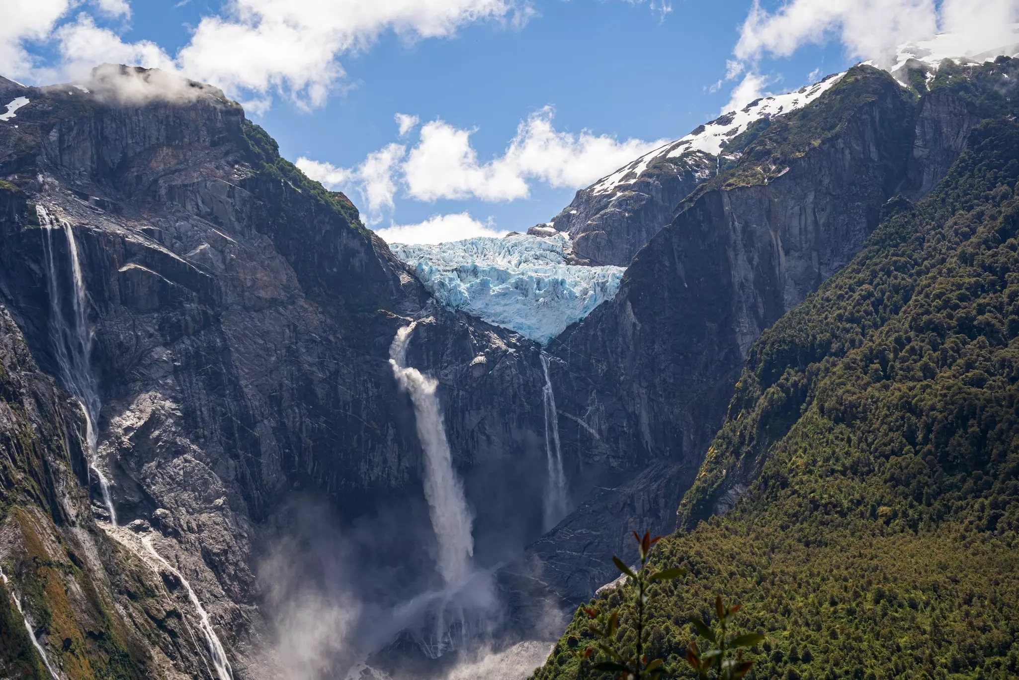 A glacier above high cliffs in a mountain setting, with waterfalls descending from the glacier.