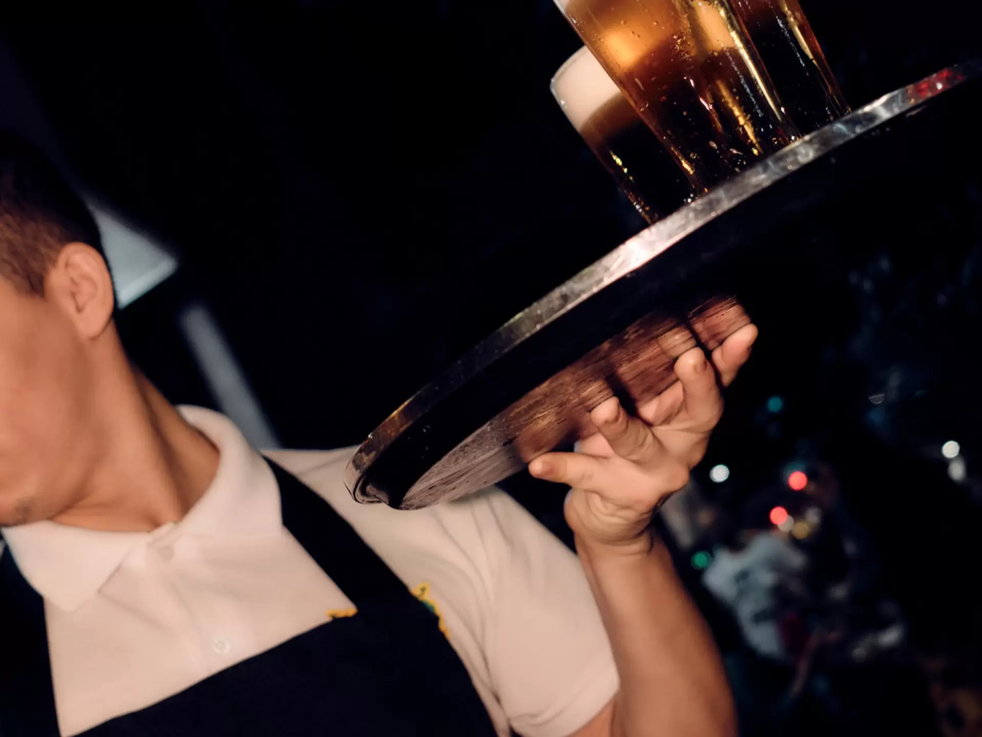 A man holding glasses of beer on a tray.