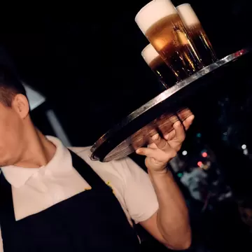 A man holding glasses of beer on a tray.