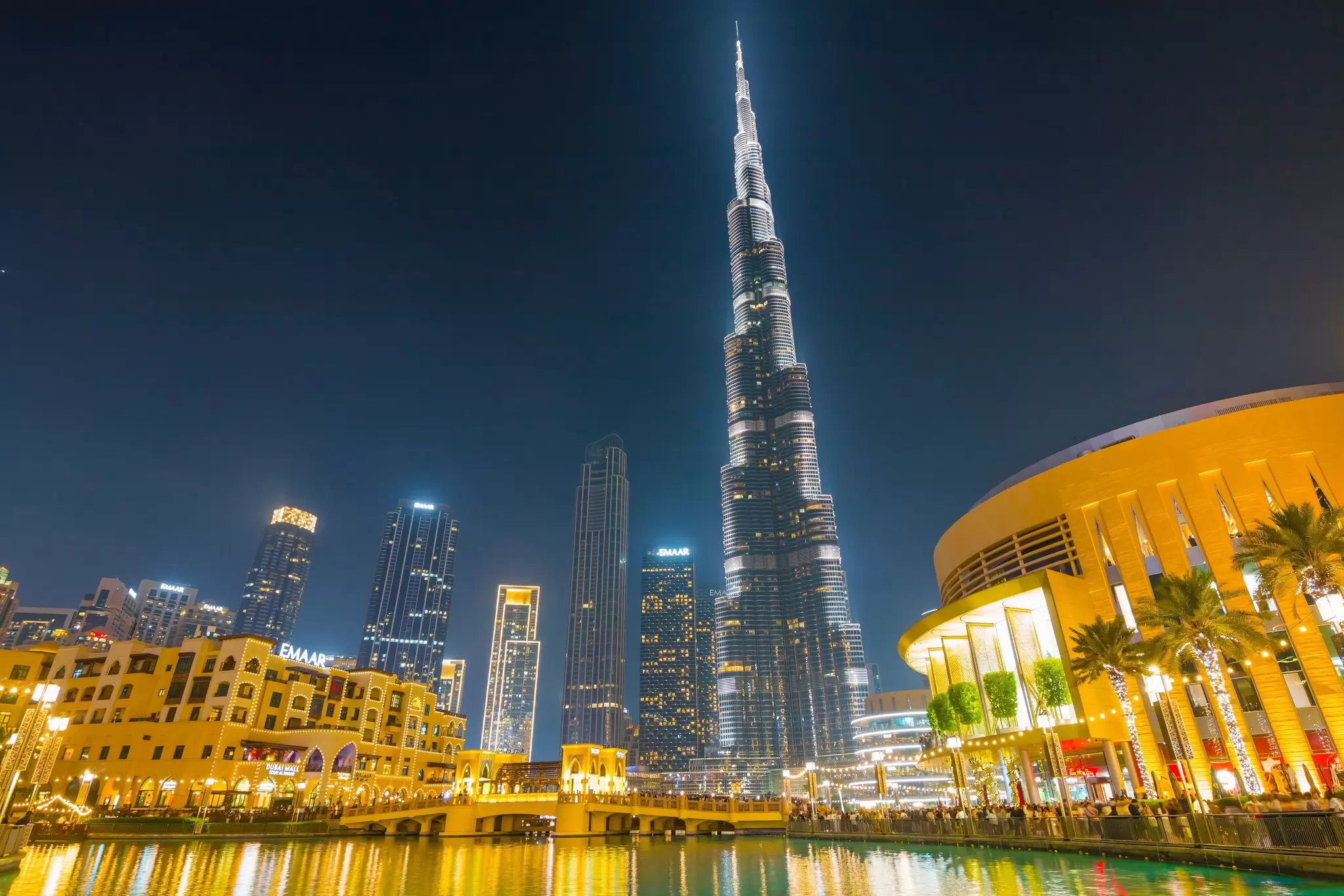 A skyscraper stretching high into the sky above some low-rise waterfront buildings: the Burj Khalifa at night. 