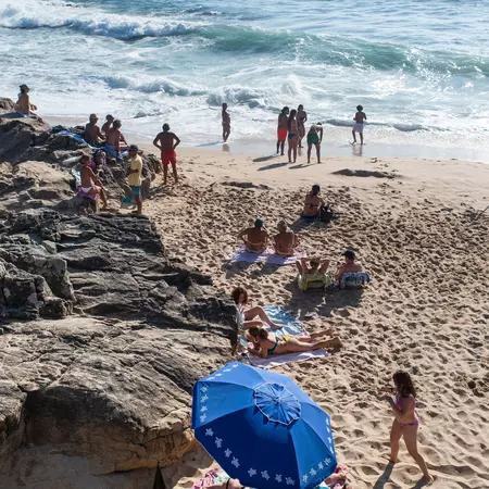 An overhead view of people on a beach; there is a a large blue sun umbrella in the foreground.