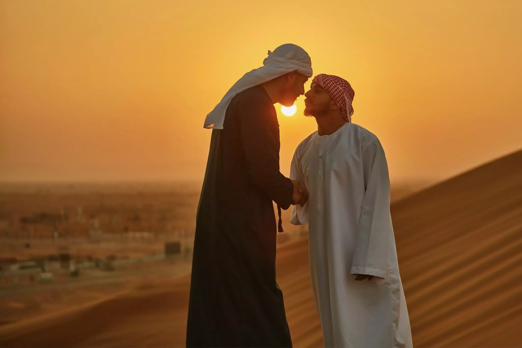 Middle Eastern men greeting each other with a handshake and nose rub in the desert at sunrise