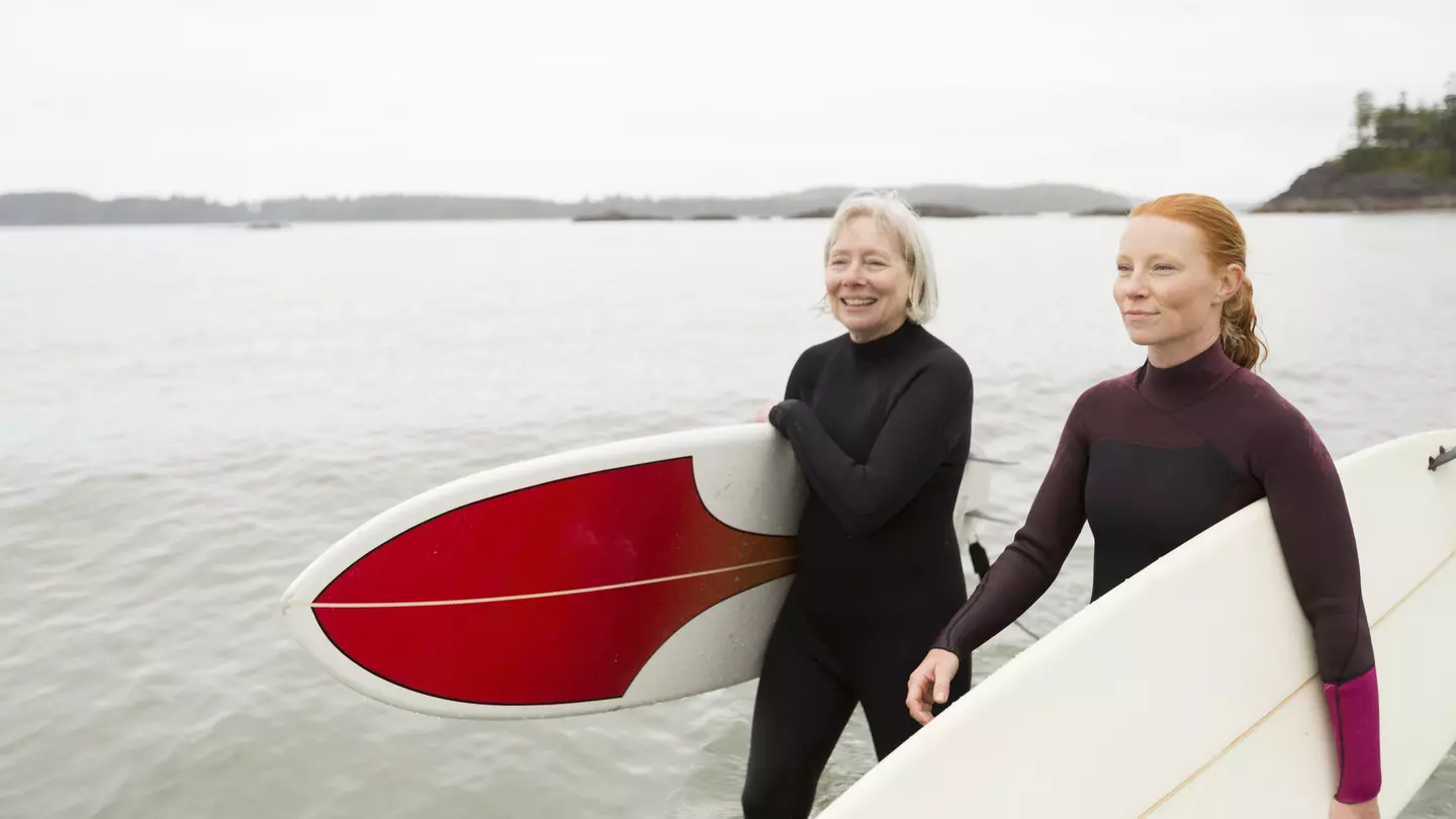 Two surfers carrying boards walk along a beach smiling