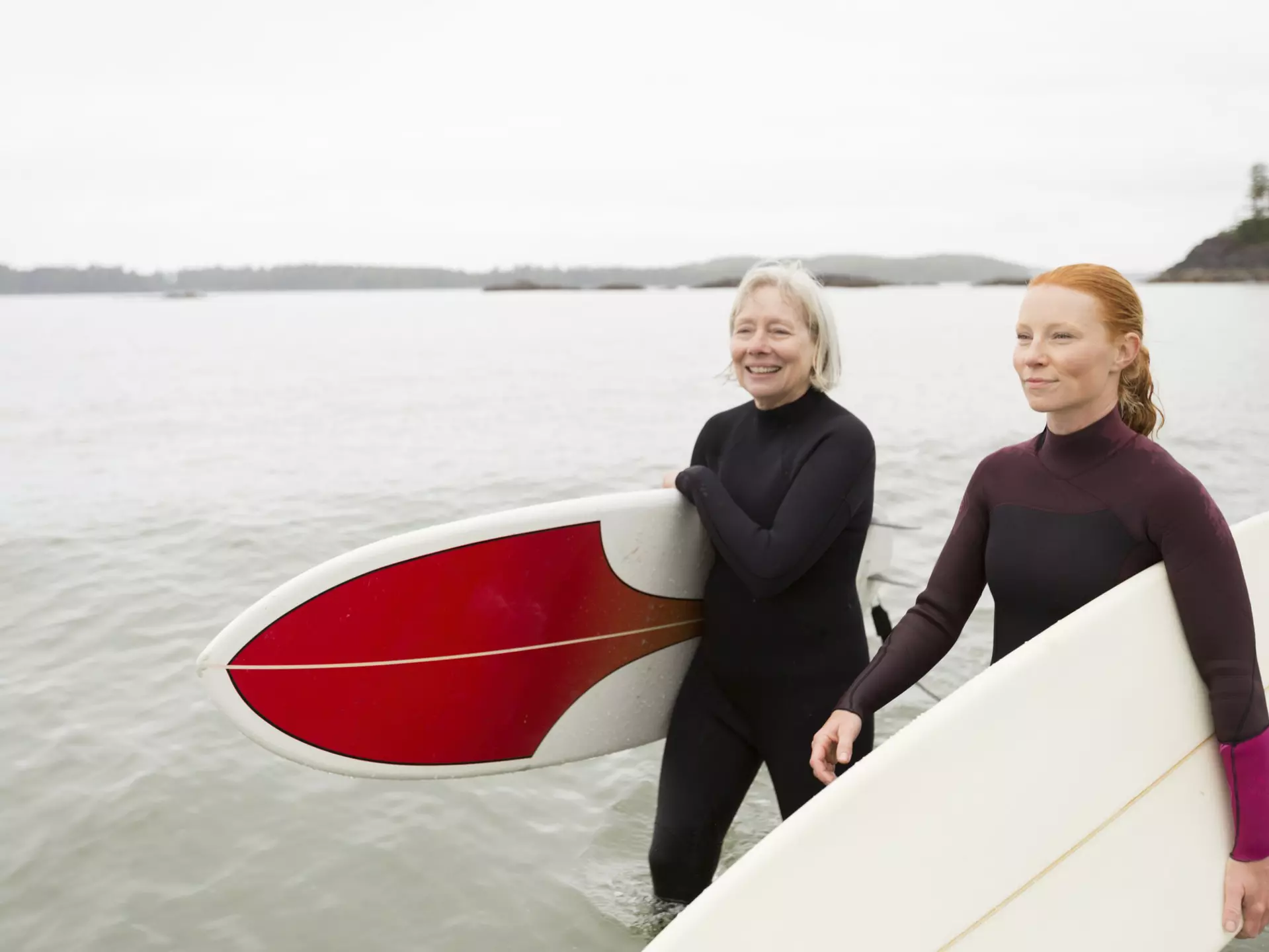Two surfers carrying boards walk along a beach smiling