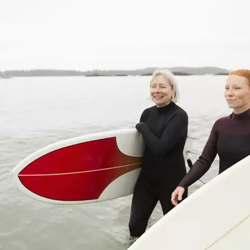 Two surfers carrying boards walk along a beach smiling