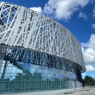Low-angle view of a curved museum with a white interlaced metal lattice over a dark glass wall, palm trees and blue sky