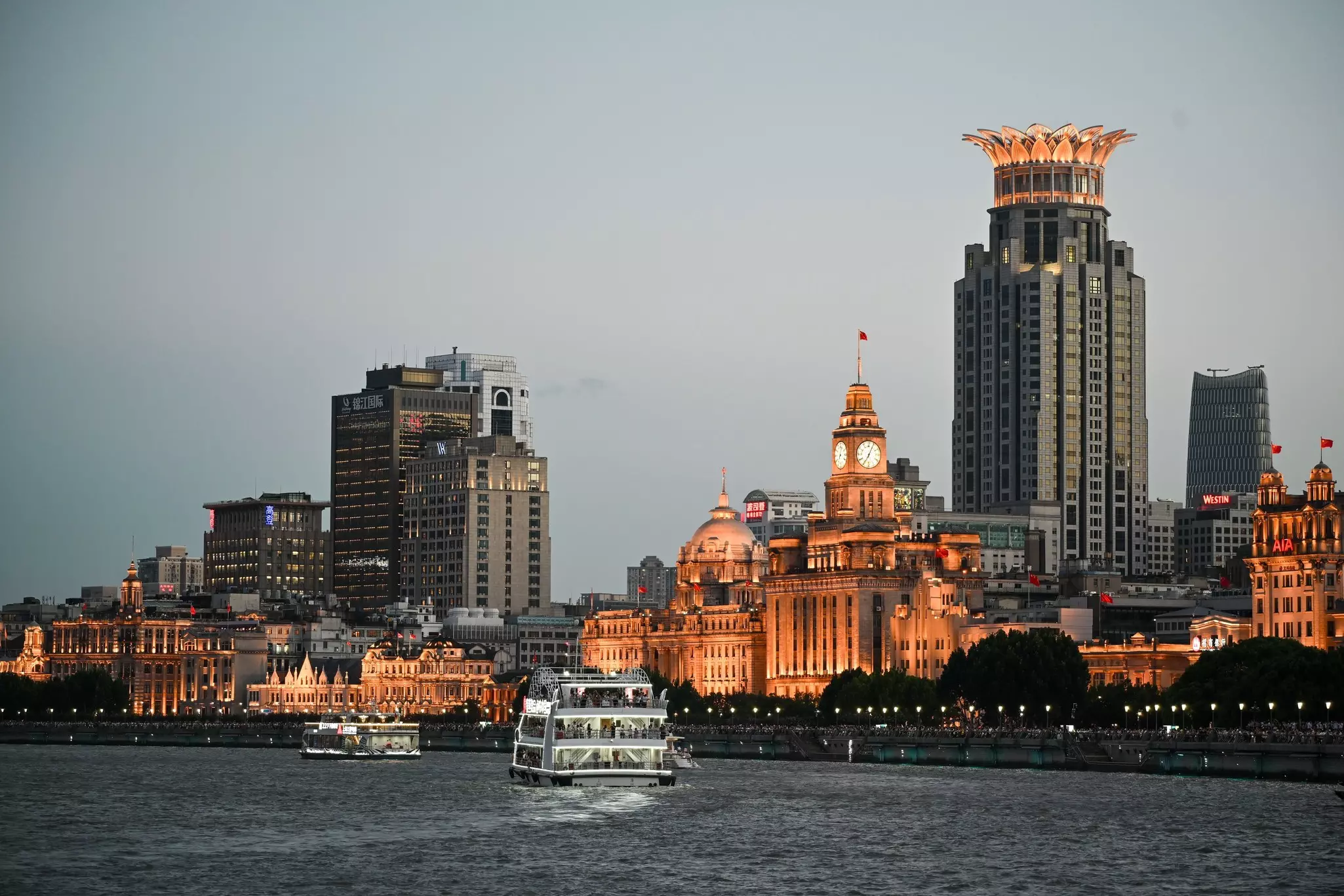 A ferry approaches the dock at a waterfront lined with European-style architecture, including a domed building and a clock tower.