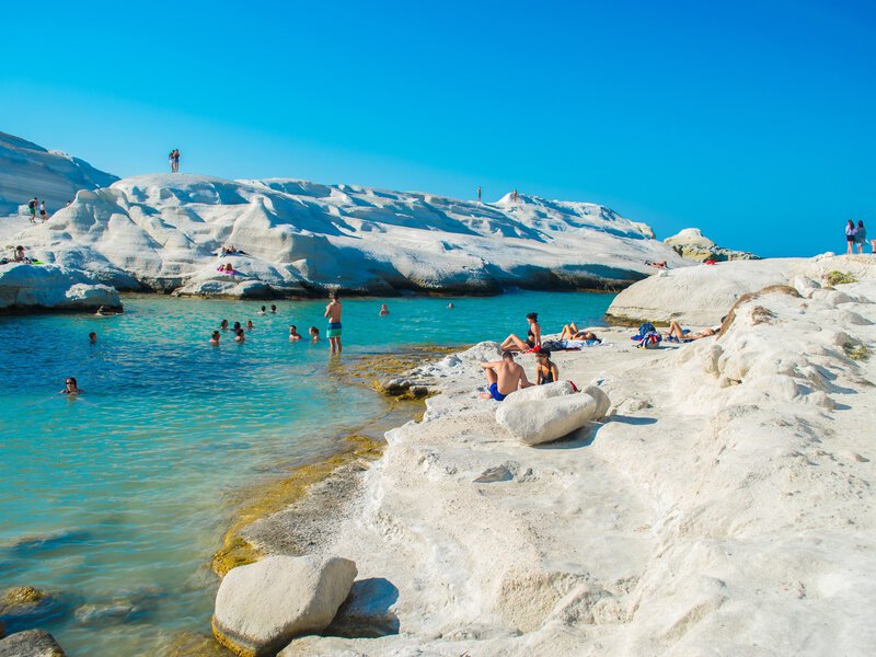 August, 2018: Swimmers and sunbathers at Sarakiniko beach with white volcanic rocks.