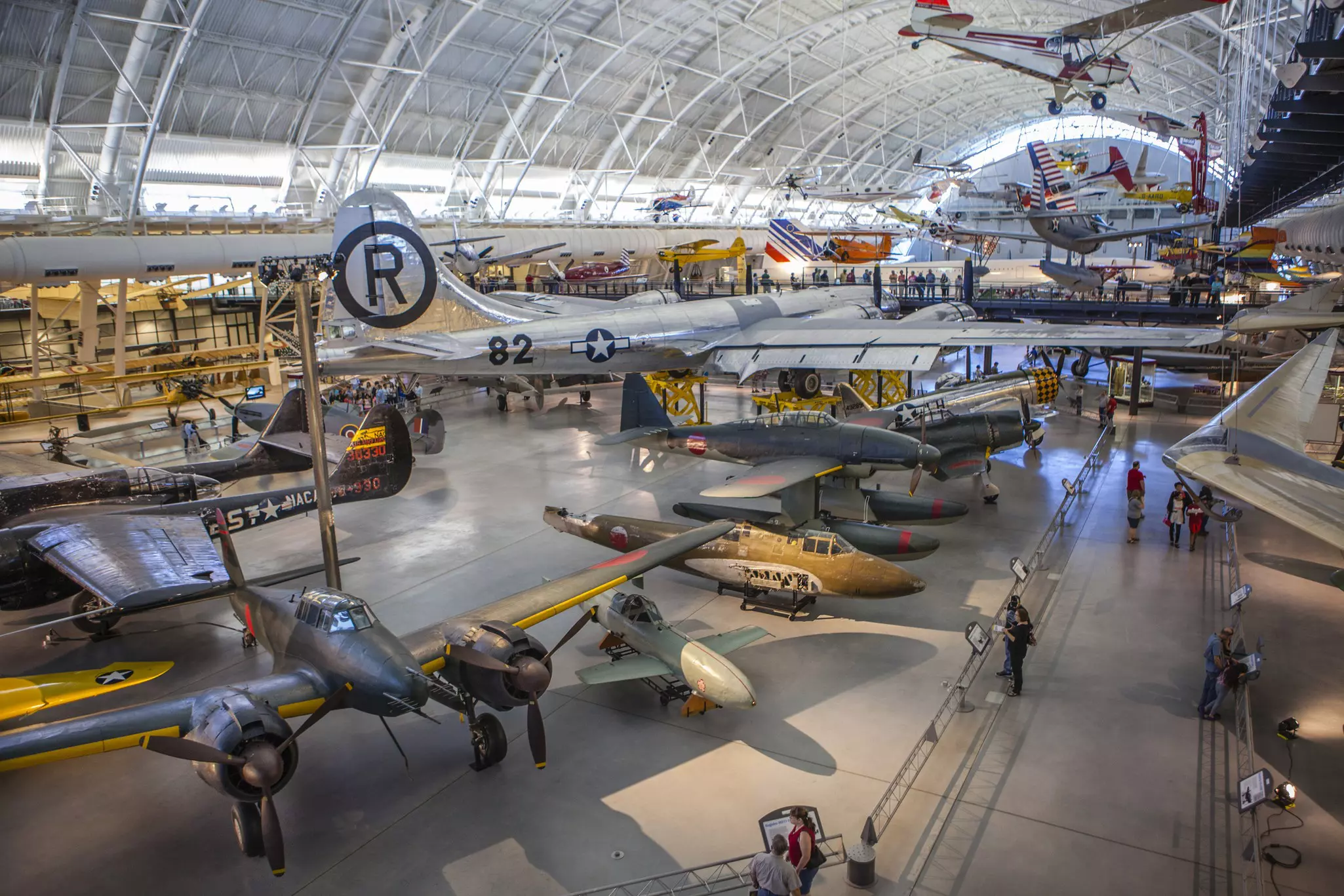 A huge aircraft hangar displaying many different types of plane, rocket and engine. People are following the walkways between exhibits