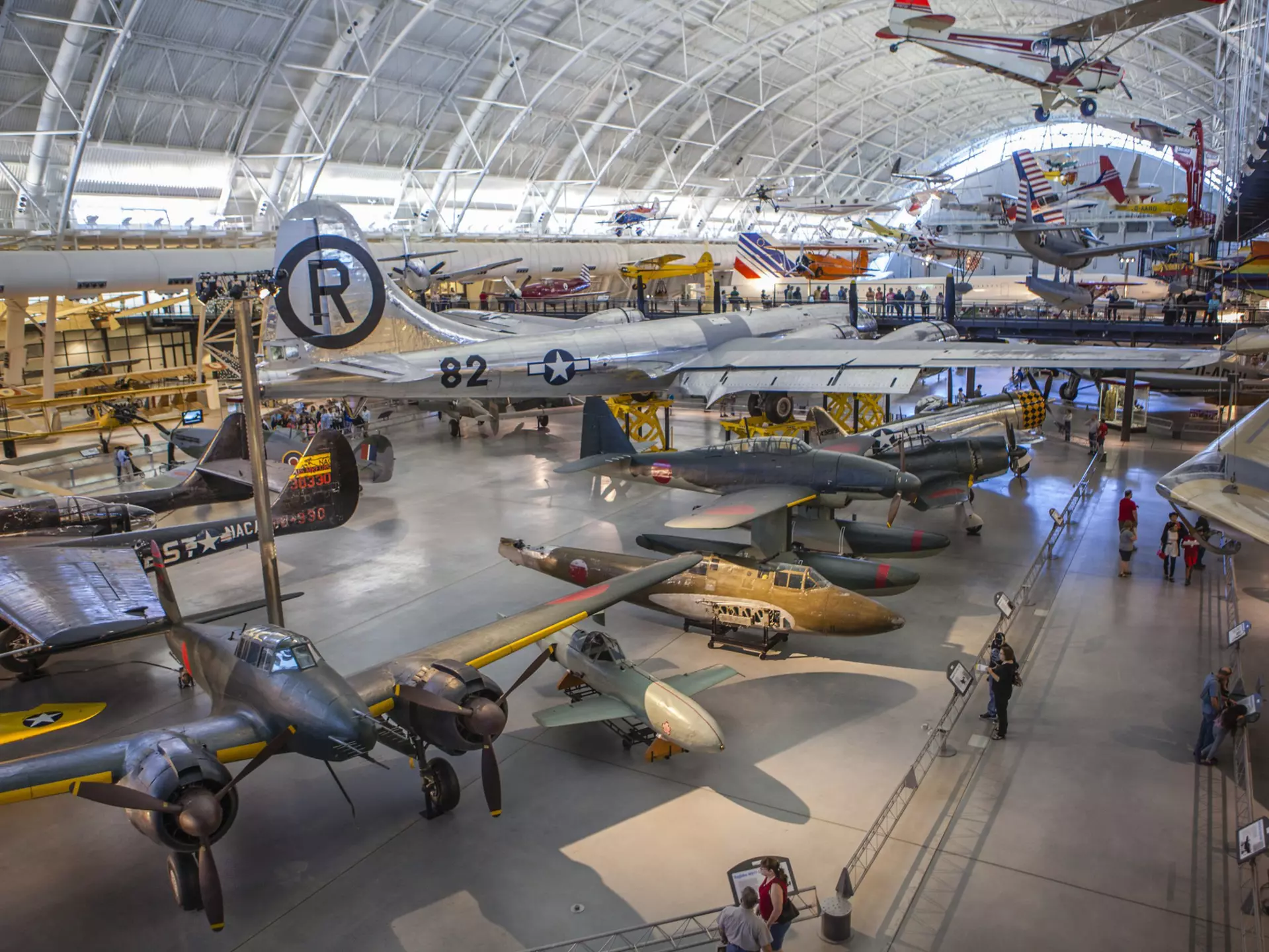 A huge aircraft hangar displaying many different types of plane, rocket and engine. People are following the walkways between exhibits