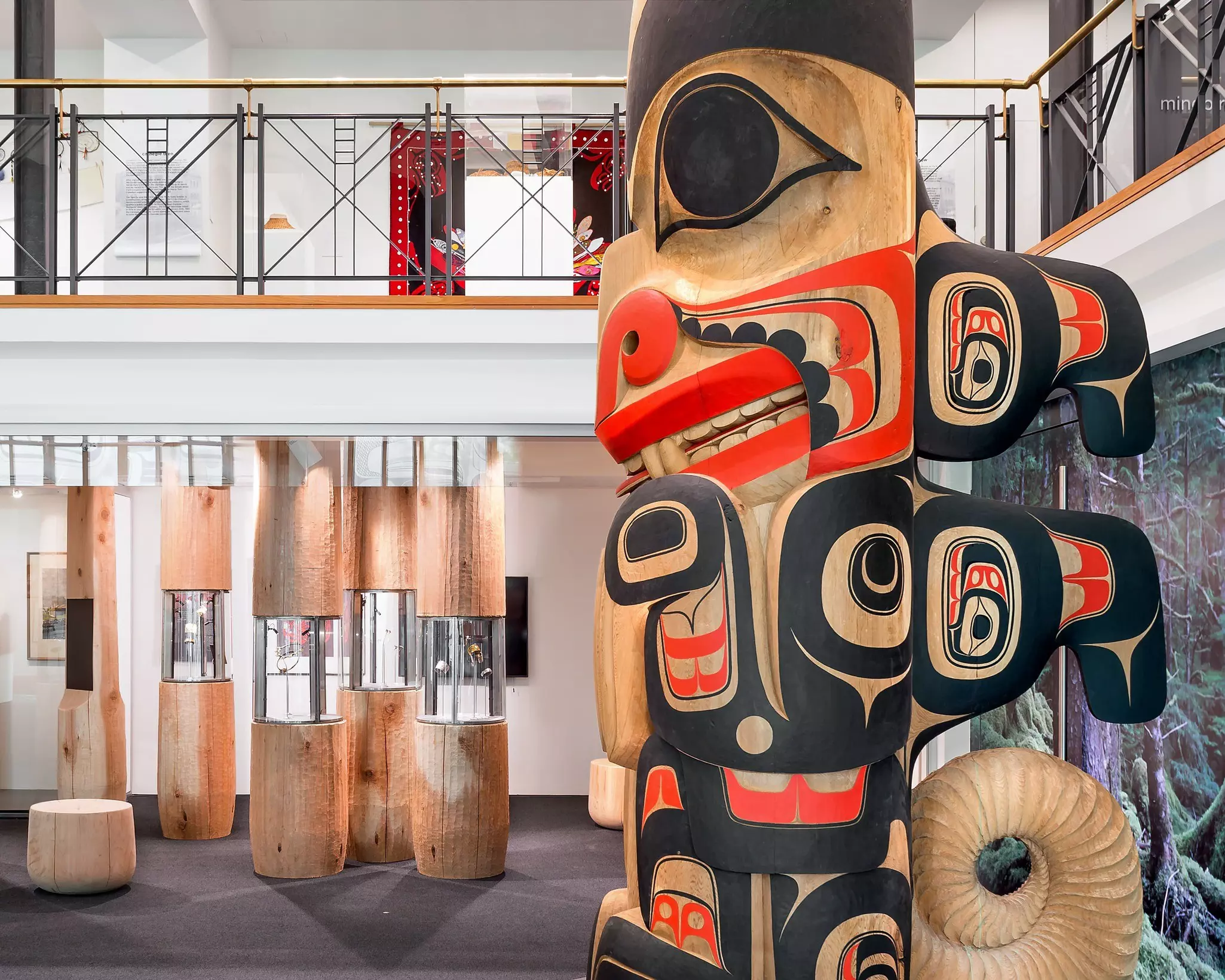 Colorful Indigenous art, including a totem pole and carved wooden-and-glass display cases, inside a brightly lit gallery.