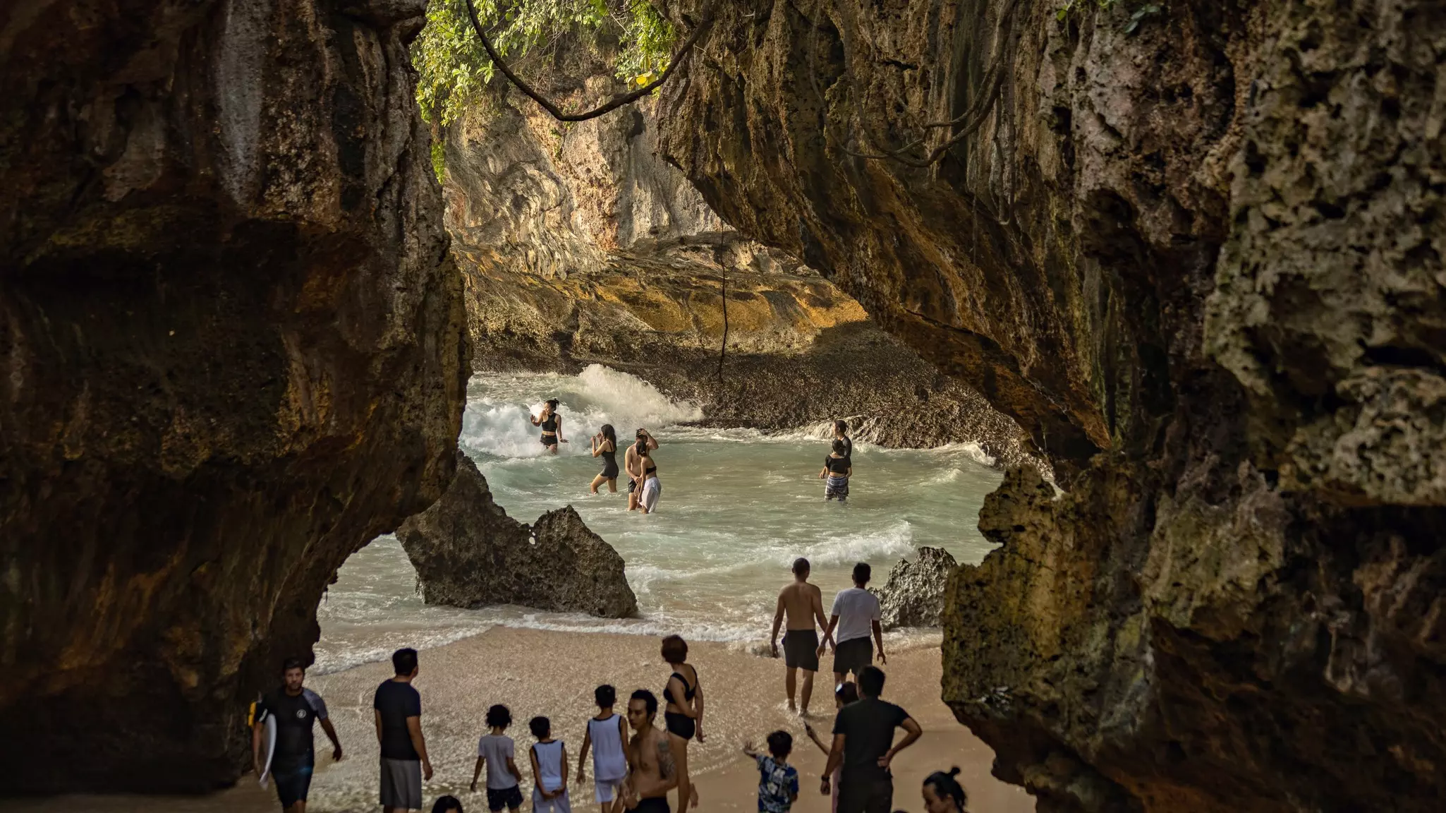 A view through the rocky cliffs of people at Uluwatu beach in Bali, Indonesia. 