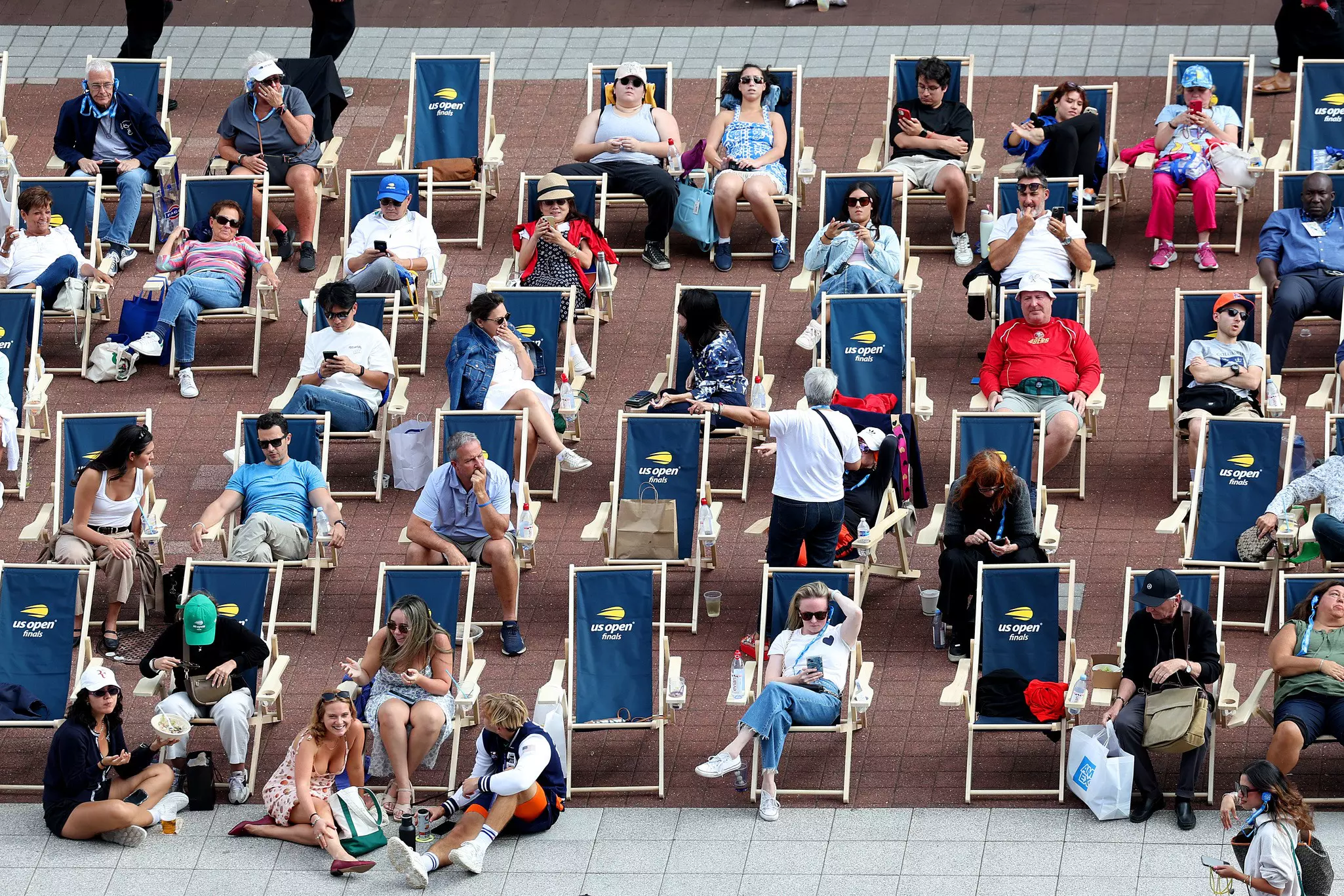 Tennis fans sitting in lines of deckchairs with a "US Open" logo on them.