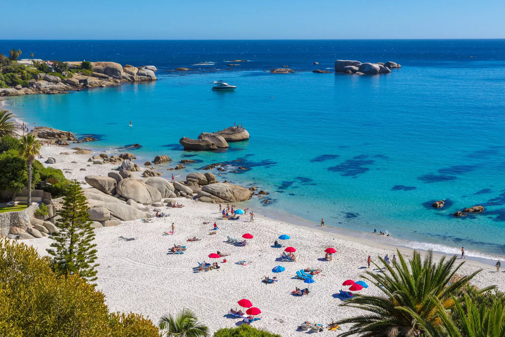 A busy sandy beach, with people under colorful sunshades.