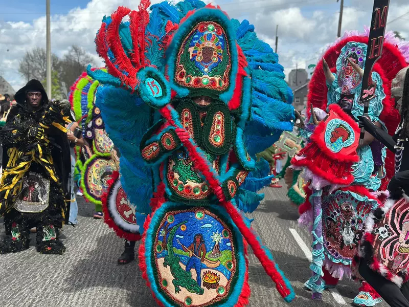 People in elaborately beaded, colorful costumes with feathers in a parade.