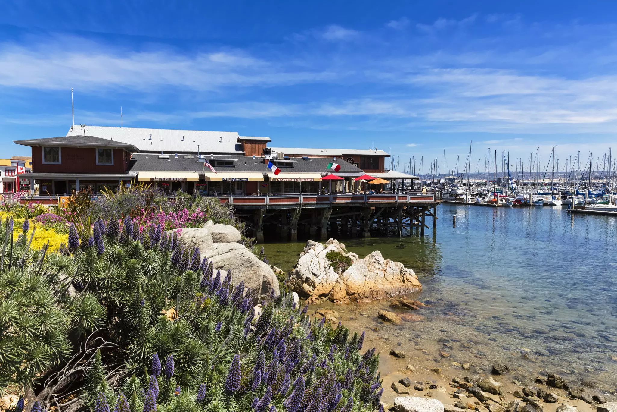 Cannery Wharf in Monterey is seen with a view of several sailboats tied up and the bay stretching out beyond