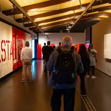 People walking through a museum hall lined with large red graphic panels of text.