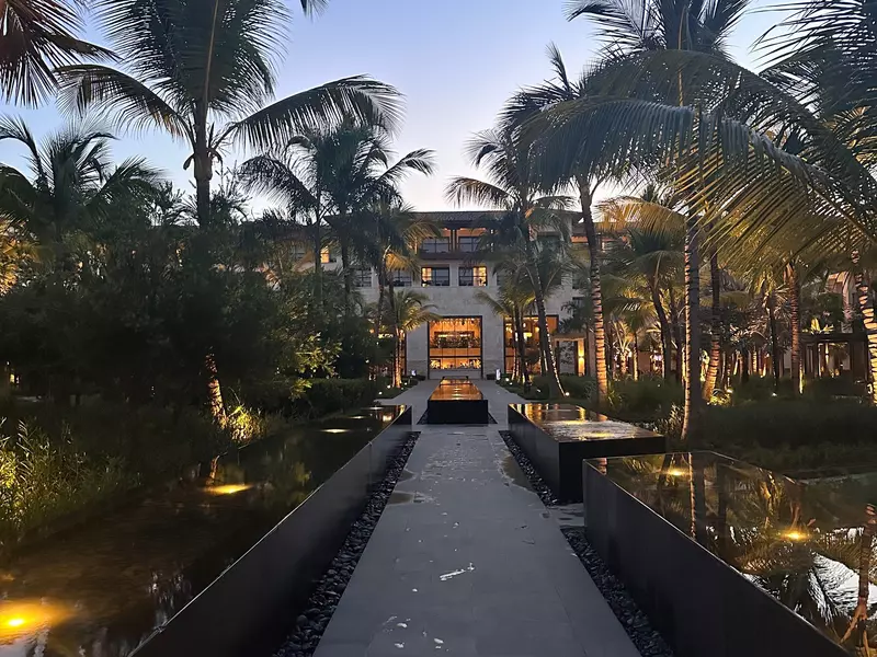 Palm trees line a pathway to the large open doorway at a resort.
