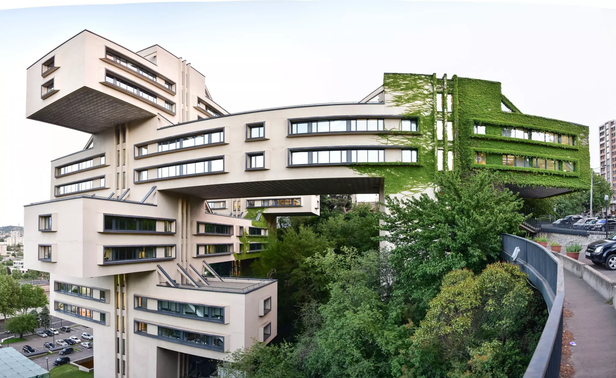 A series of large rectangular blocks stacked on and across each other to form a vast office building covered in ivy on one side.
