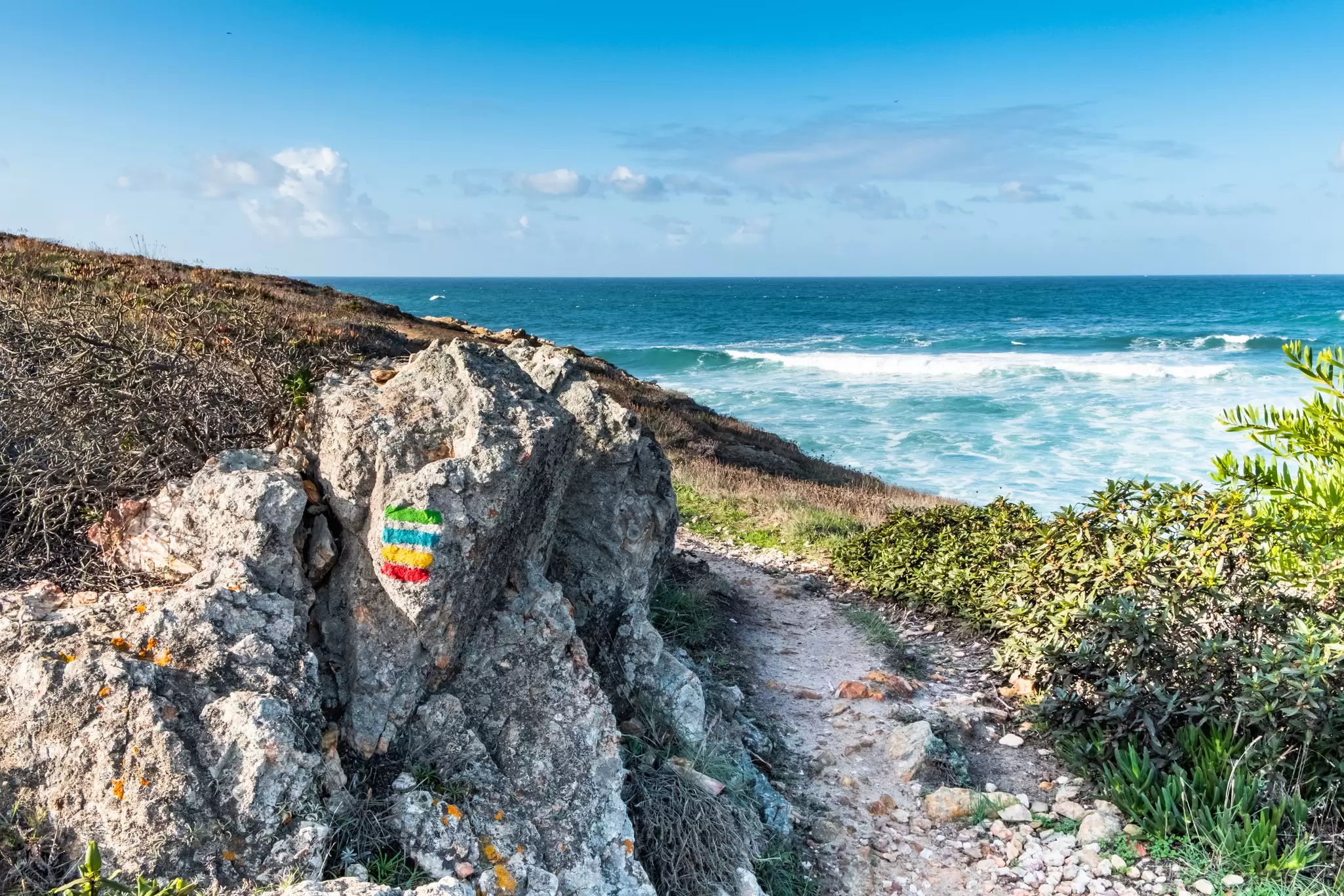 Rocks with the Rota Vicentina trekking sign, with the ocean in the background, in Portugal.