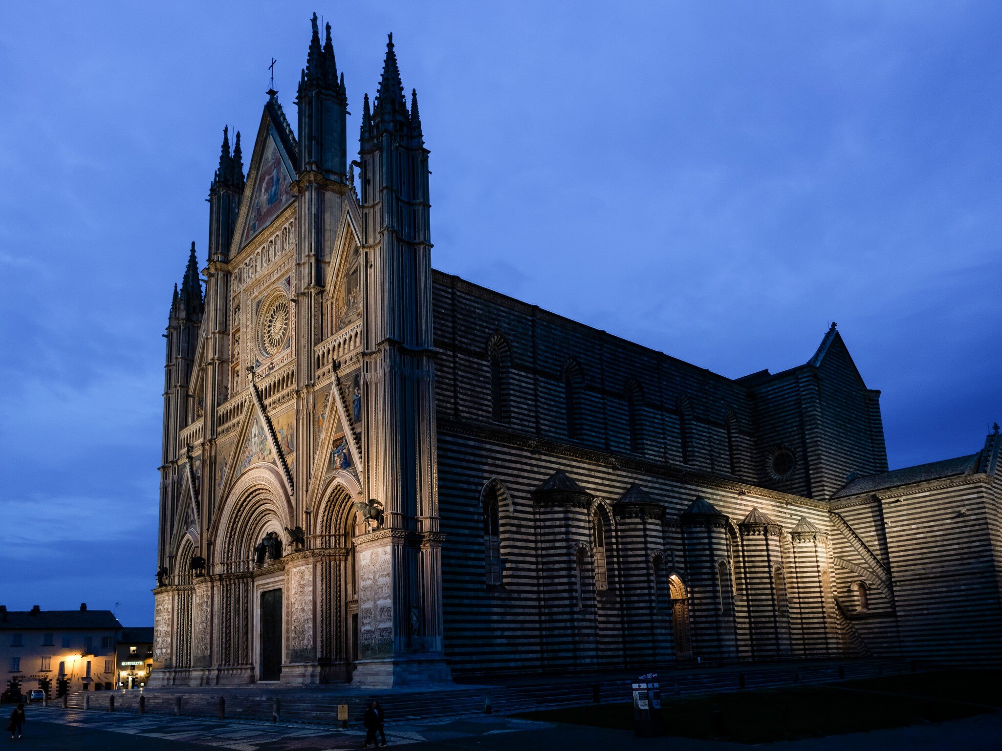 Orvieto's Gothic cathedral under a deep blue evening sky, its spired front and striped side wall lit against the dark.
