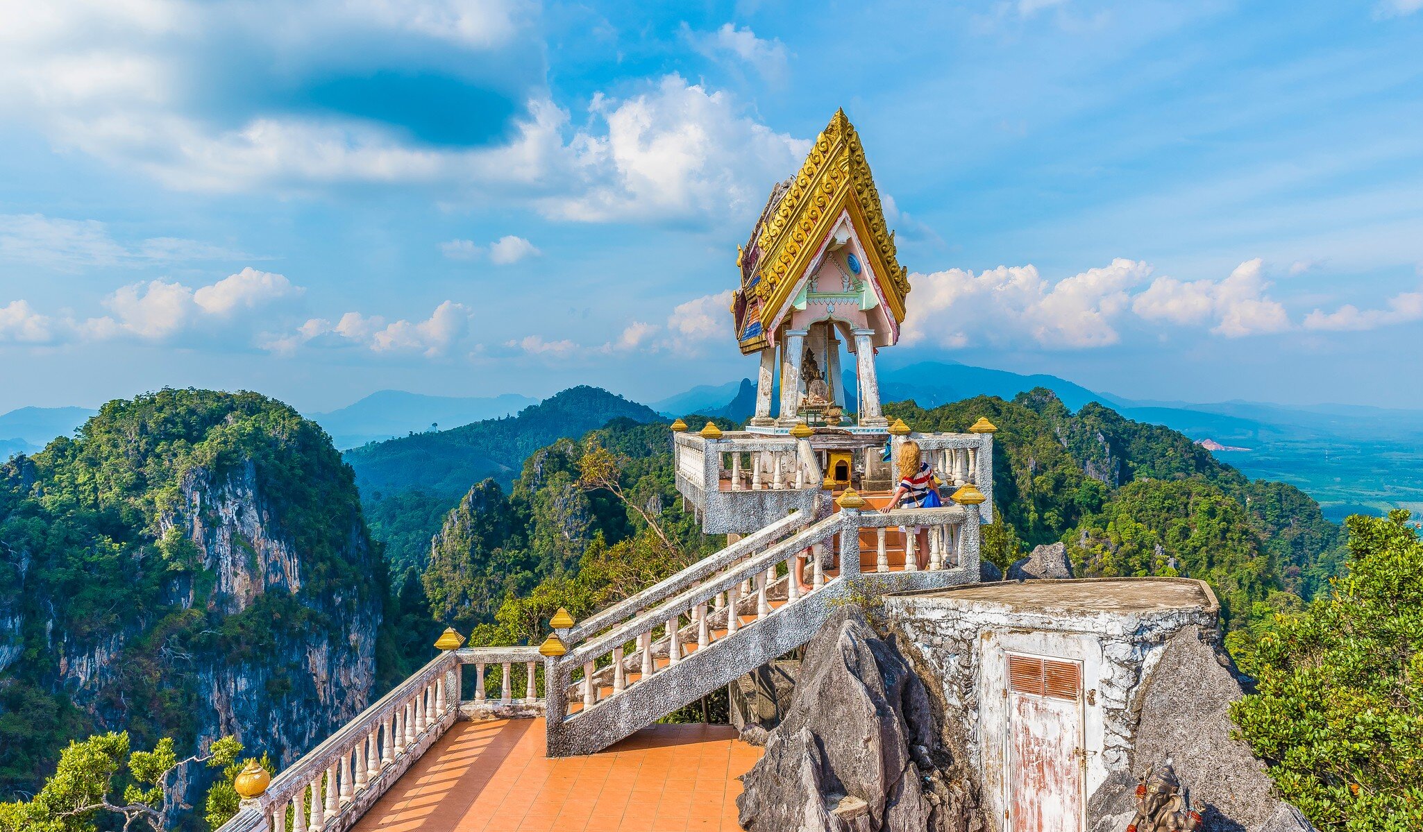 The top of Tiger Cave temple, (Wat Tham Suea), Krabi region, Thailand. Tourist on staircase with vast mountain scene in background.