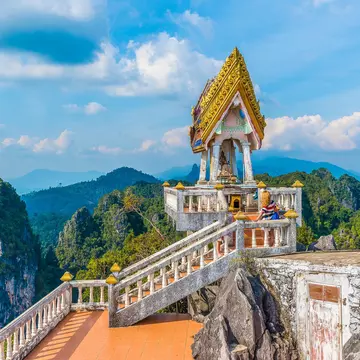The top of Tiger Cave temple, (Wat Tham Suea), Krabi region, Thailand. Tourist on staircase with vast mountain scene in background.