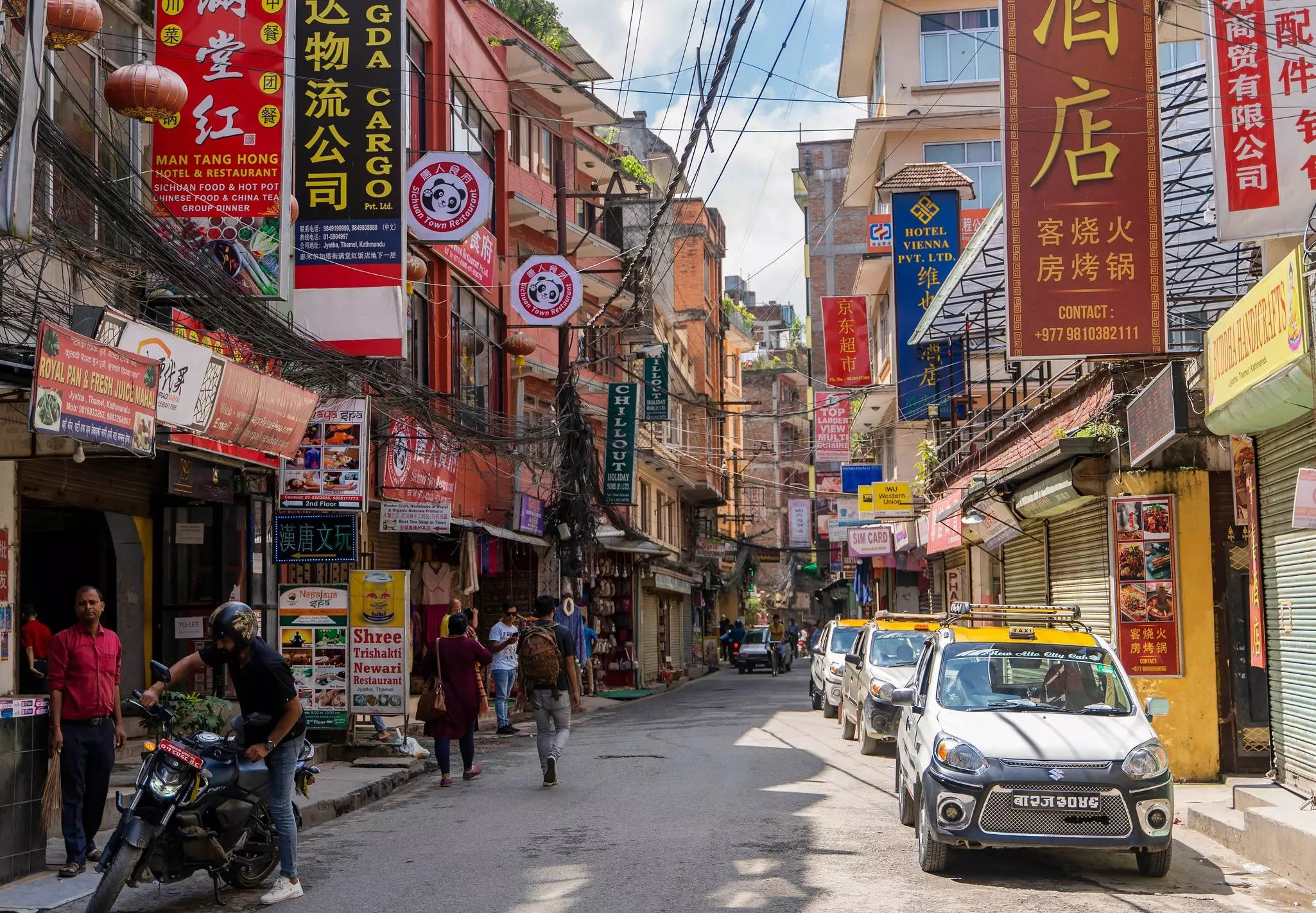 A narrow street with rows of buildings that have signs in Chinese and English