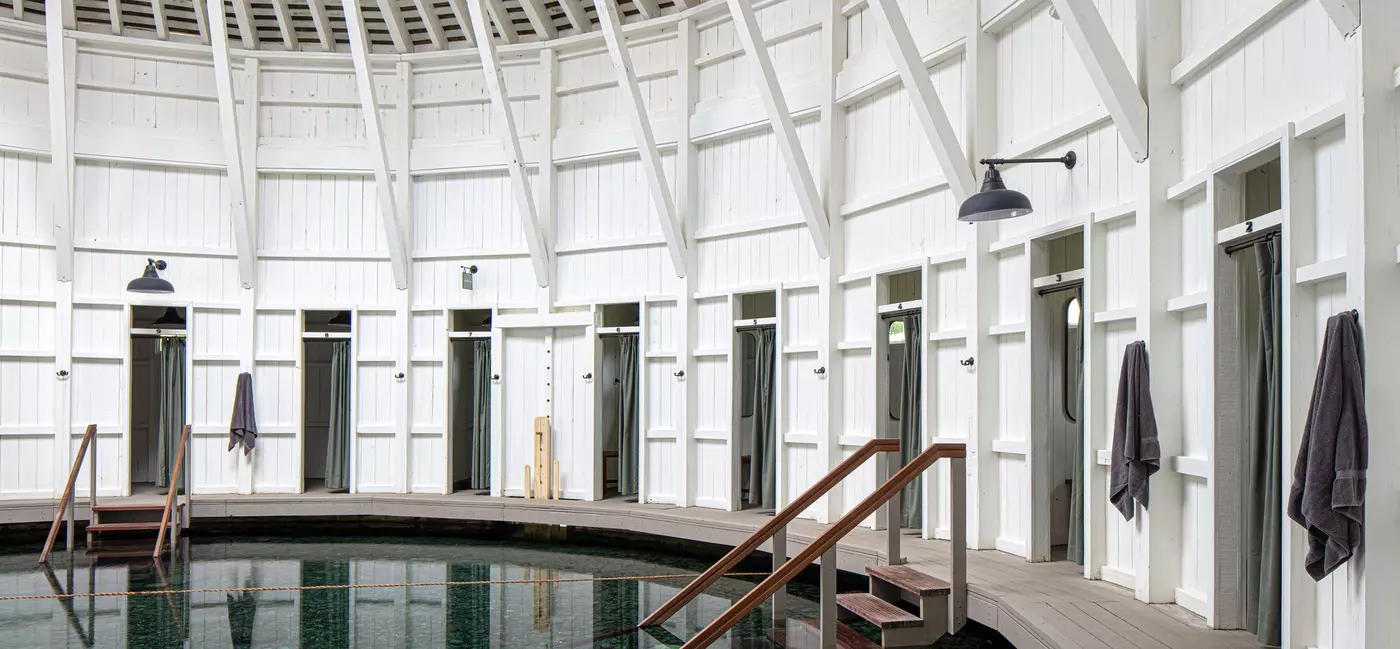 An indoor warm spring inside a round white wooden building, with dressing rooms lining the outer edge