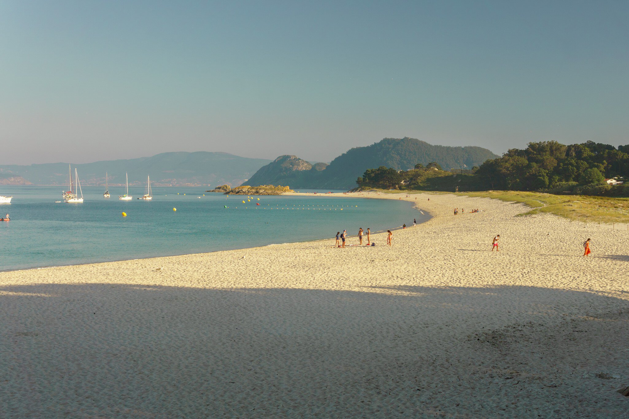 People at sandy beach in the late afternoon with strong shadows on the sand.