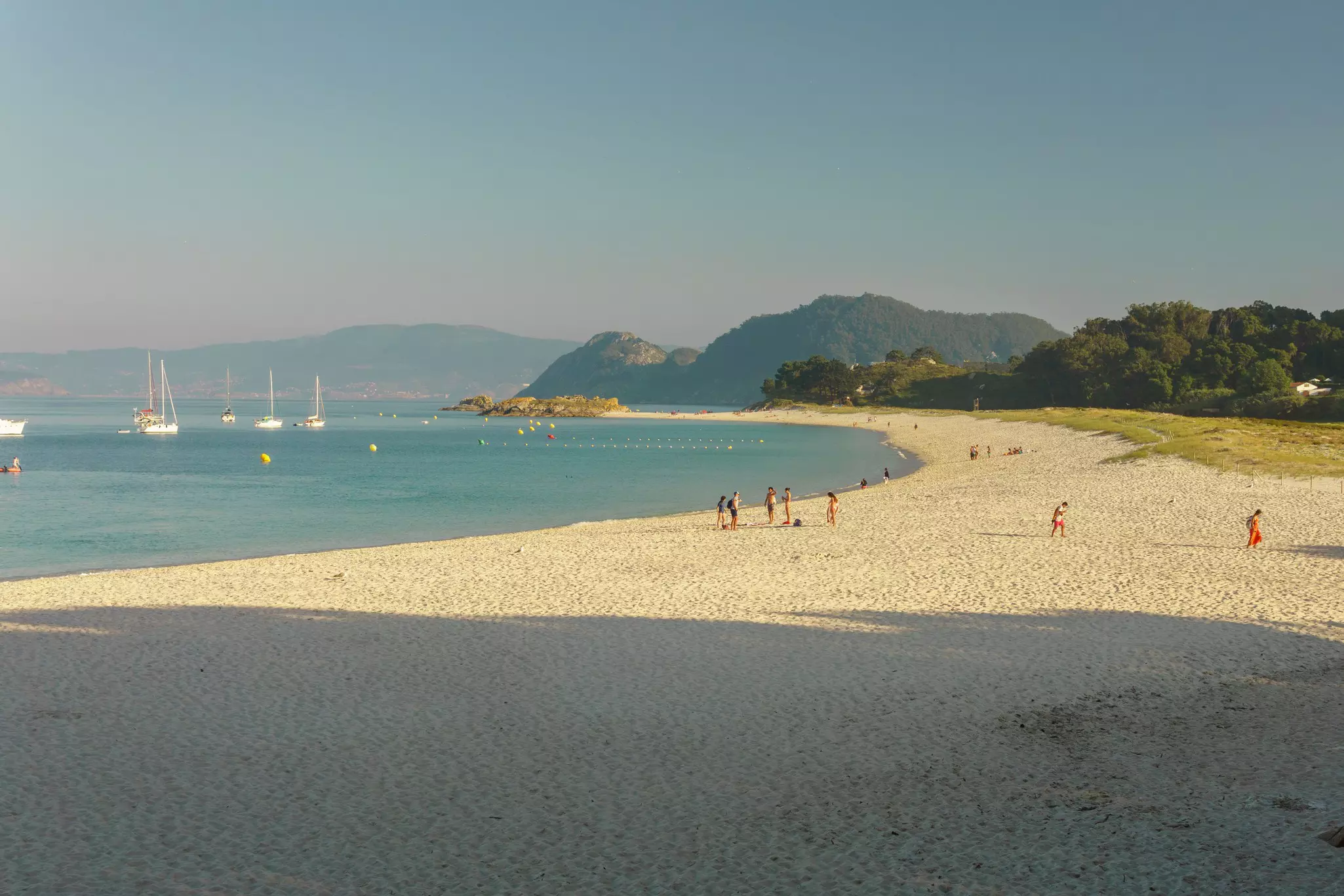 People at sandy beach in the late afternoon with strong shadows on the sand.