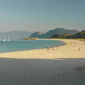 People at sandy beach in the late afternoon with strong shadows on the sand.