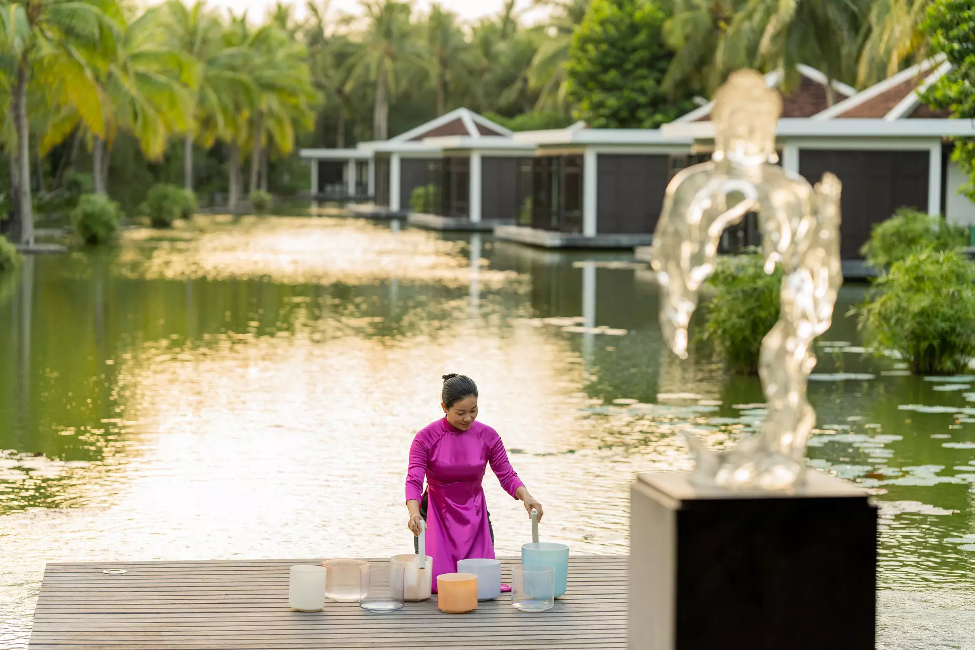 A woman touches jars by a lotus pond at a luxury resort.