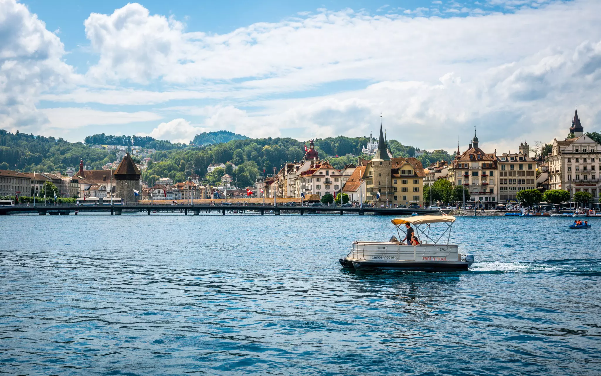 Tourists on a license free boat to rent on Lucerne lake and city with landmarks such as chapel bridge in background in Lucerne old town Switzerland.