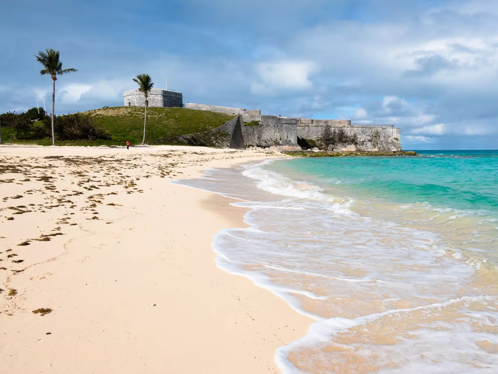 A large hilltop fort at one end of a beautiful sandy beach lapped by turquoise waves.