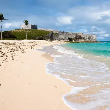 A clifftop fortress near a sandy beach lapped by clear ocean waters.