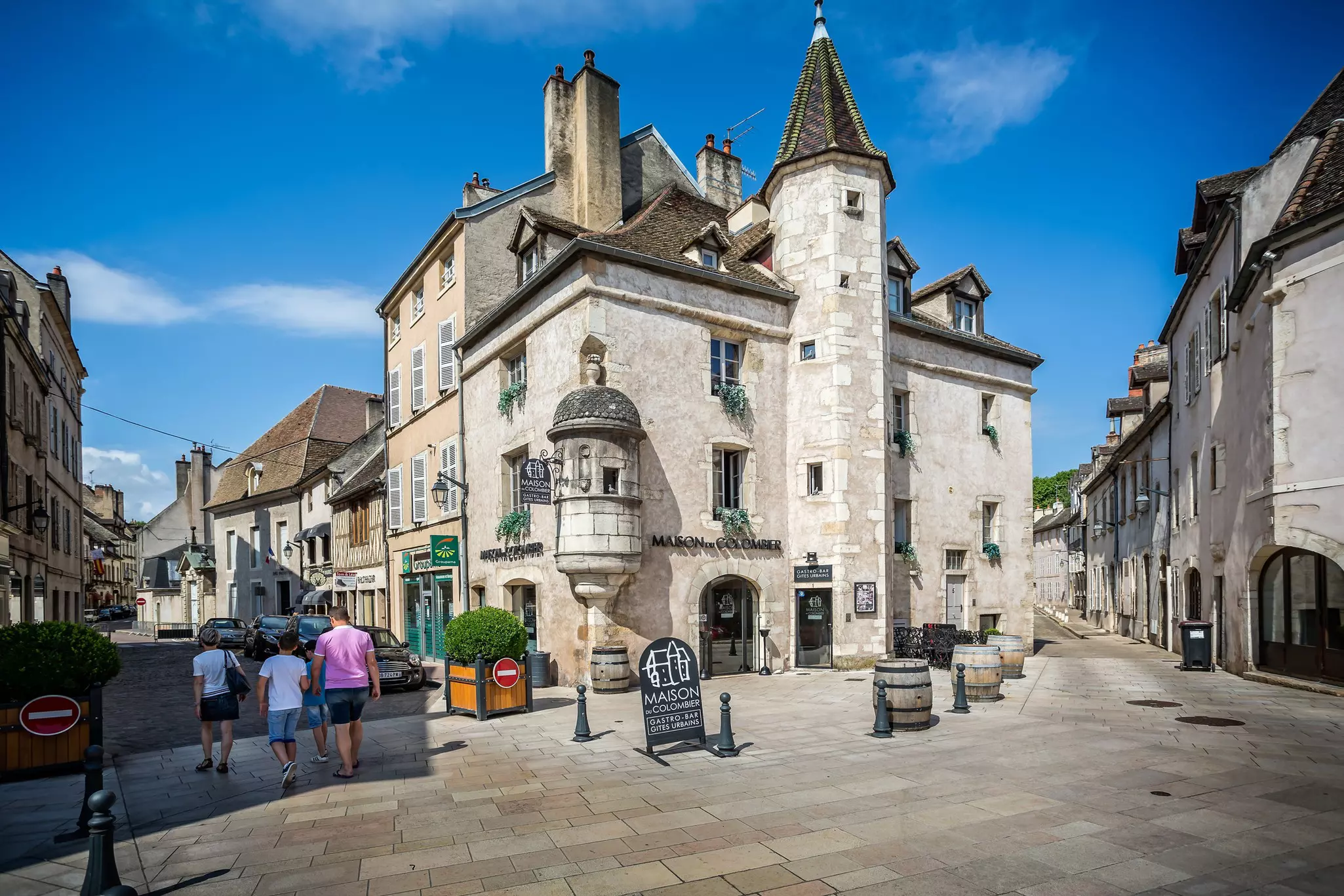 Historic streets show buildings with medieval turrets and people walking towards a restaurant.