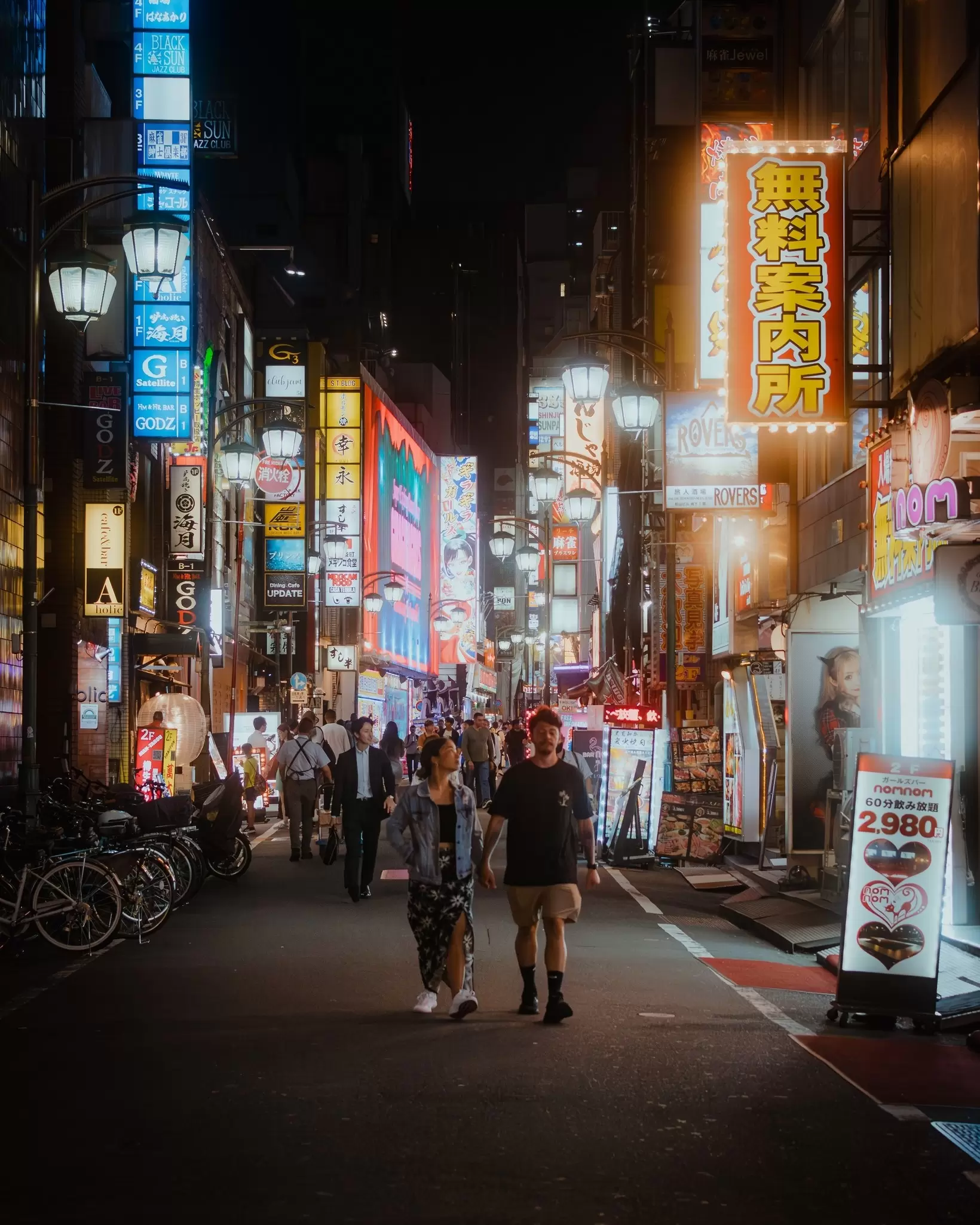 People walking at night through a pedestrian street that is brightly lit by neon signs on buildings
