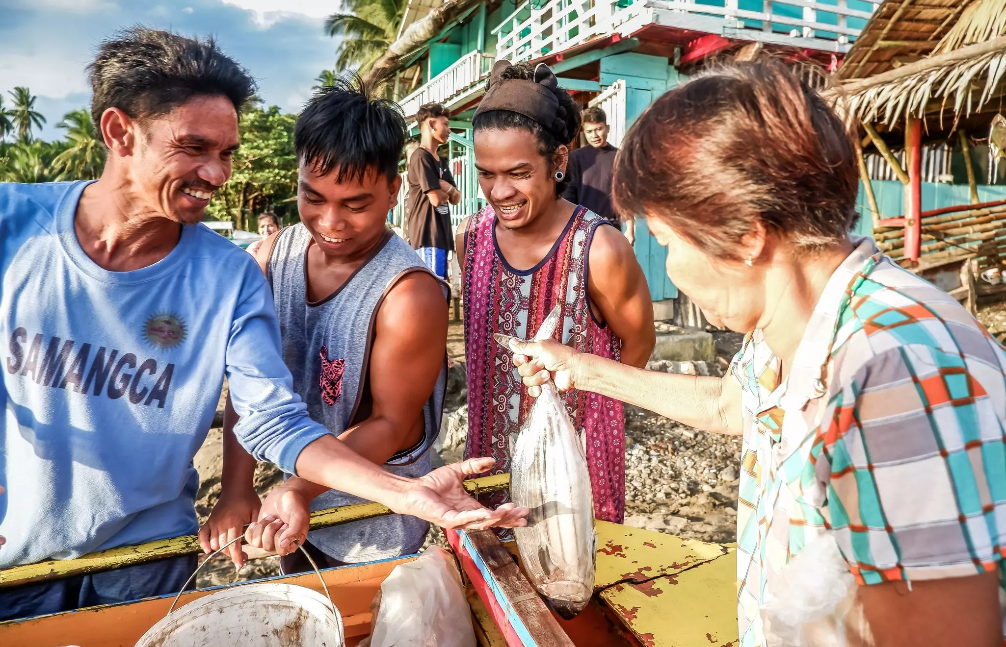 Fisherman negotiate a sale of fish to an older woman at a beach market in bright sunshine