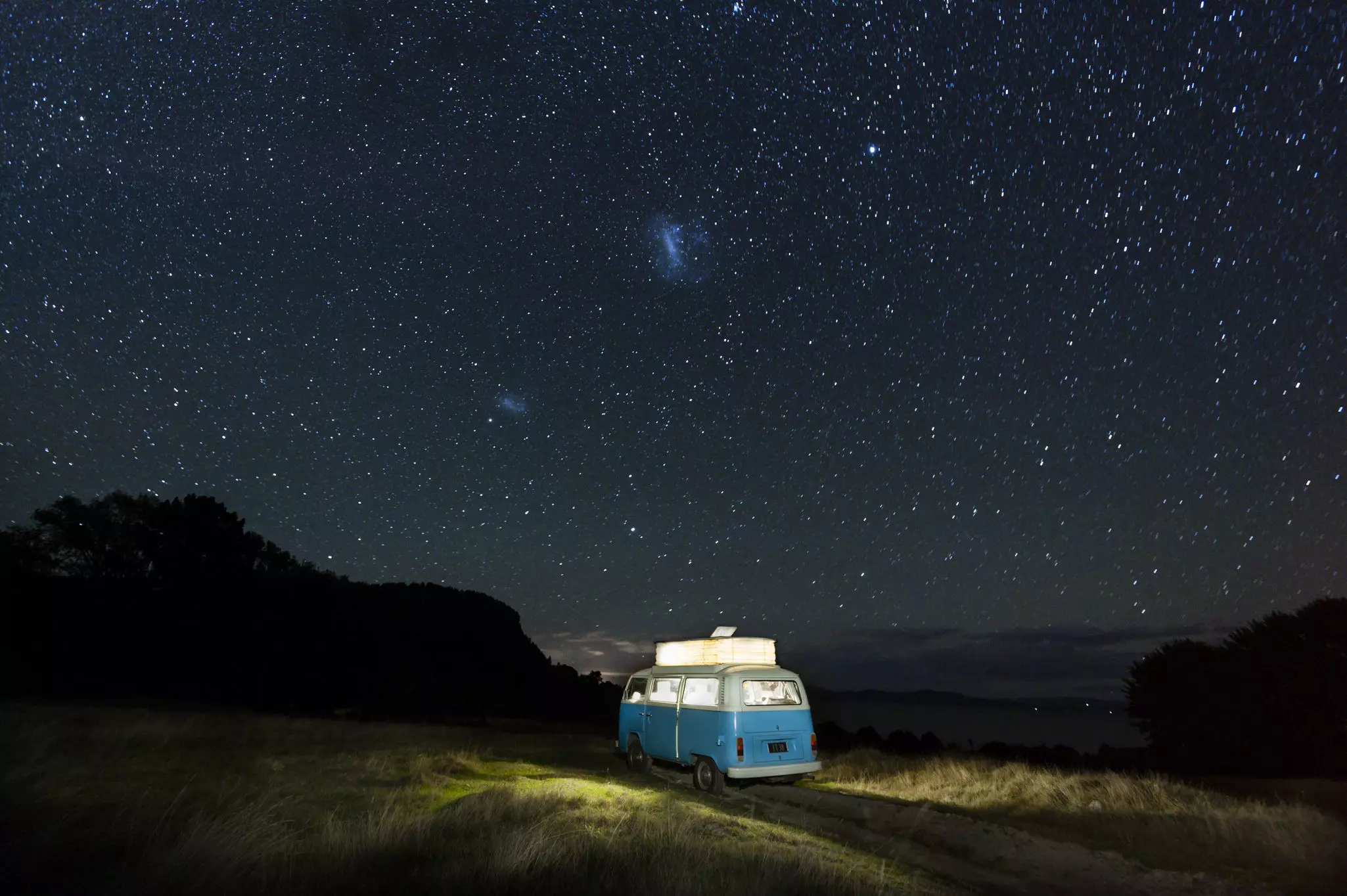 A blue campervan lit from within is parked under a starry night sky in New Zealand.