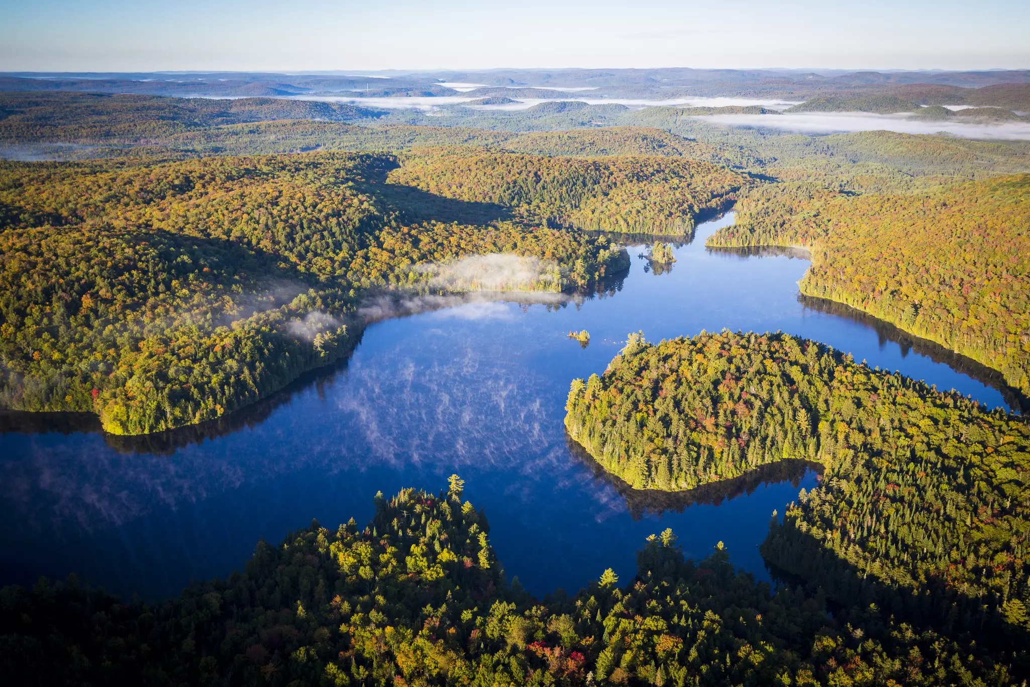 Aerial shot of dark blue water and bright green forested islands stretching out into the distance on a sunny day.