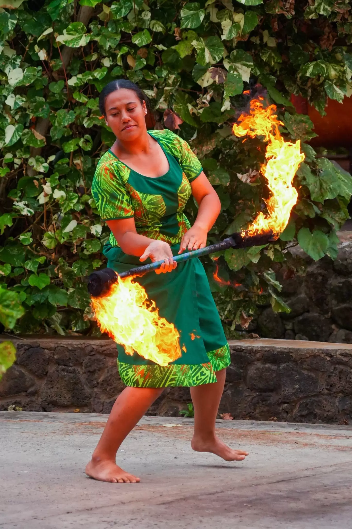 A woman in a green dress performs on stage with a flaming torch: A fire dance at the Polynesian Cultural Center, O'ahu, Hawaiʻi.