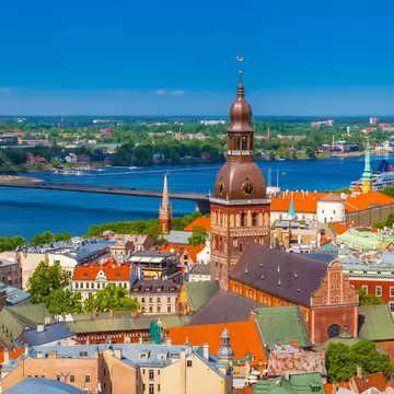 Brick cathedral with a green-brown domed tower among colourful rooftops, a wide river and cable bridge behind.