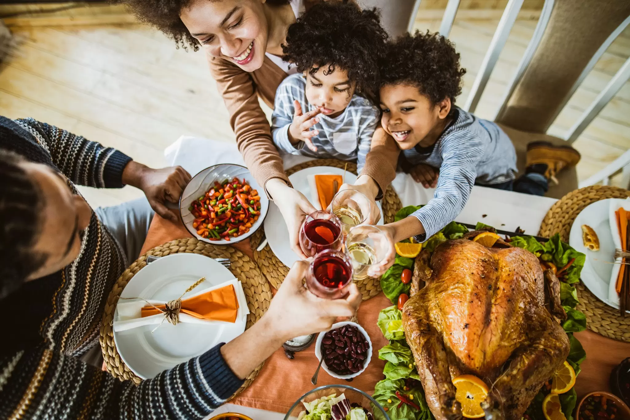Family with two children toasting drinks over a festive Thanksgiving table with roast turkey, seen from above