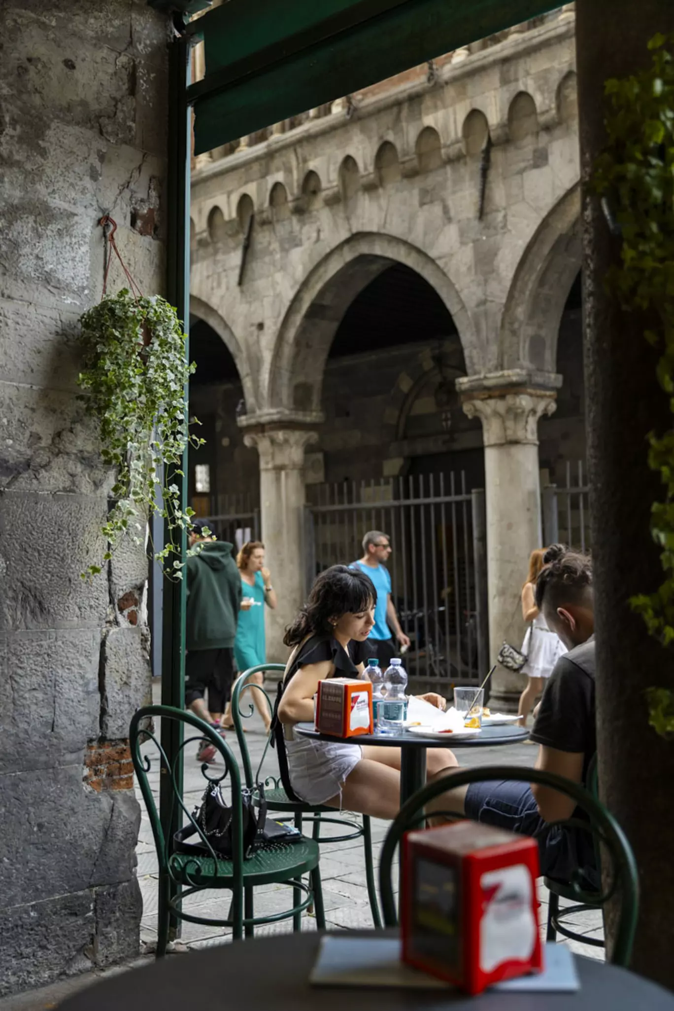 Two women sitting at the outside terrace of a small bar in a medieval alleyway.