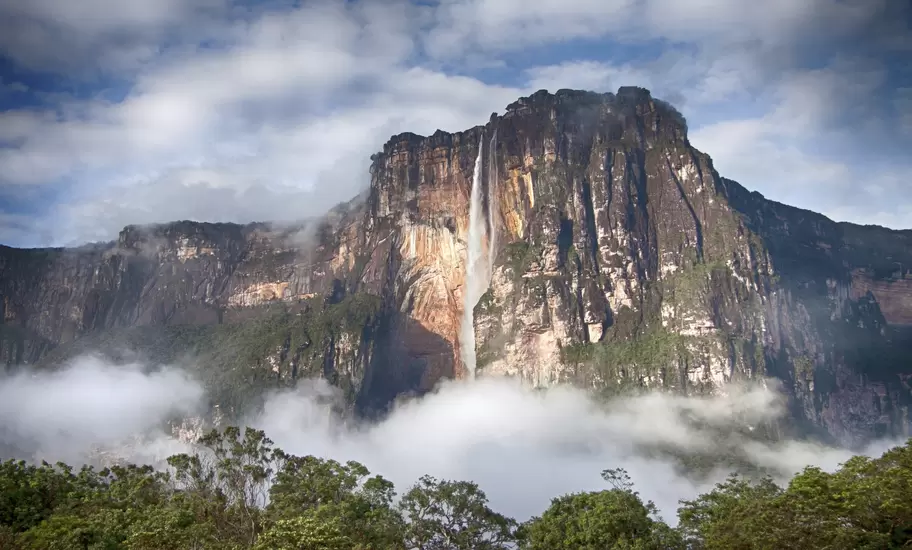 Angel Falls, Venezuela, a thin waterfall dropping down the sheer orange cliff of a tepui above low cloud and rainforest