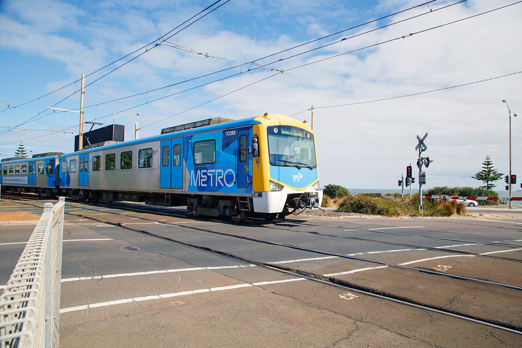 A train crosses the road as it arrives at Brighton Beach Railway Station, located on the Sandringham line in Victoria, Australia.